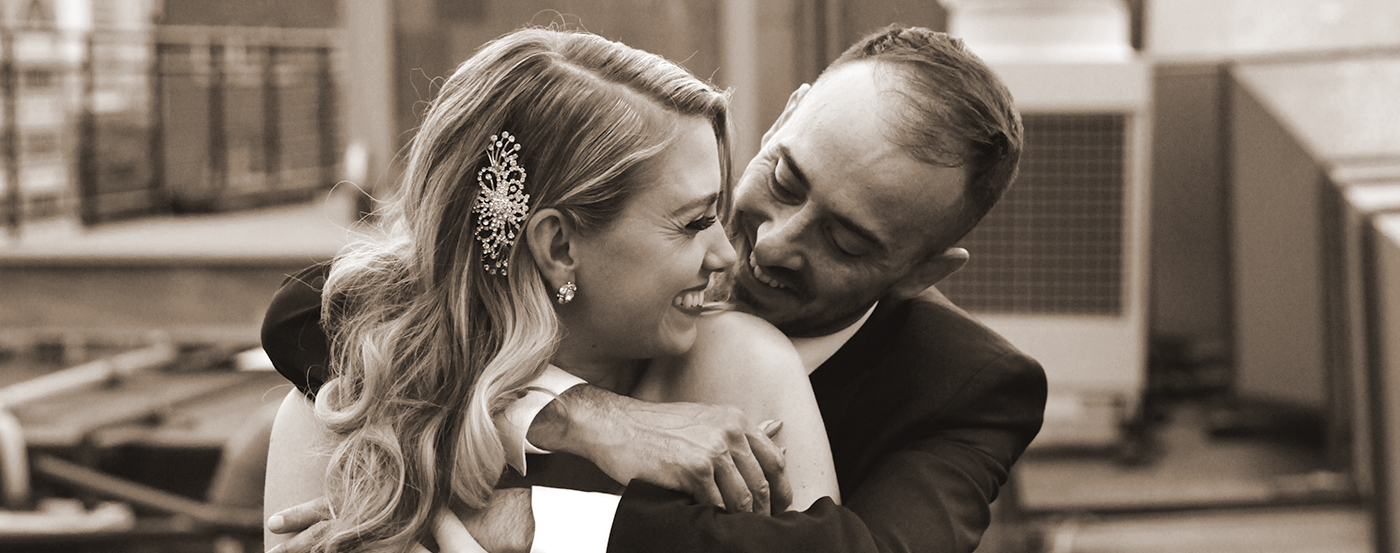 A bride wearing a dazzling barrette in her hair and being embraced by her husband.