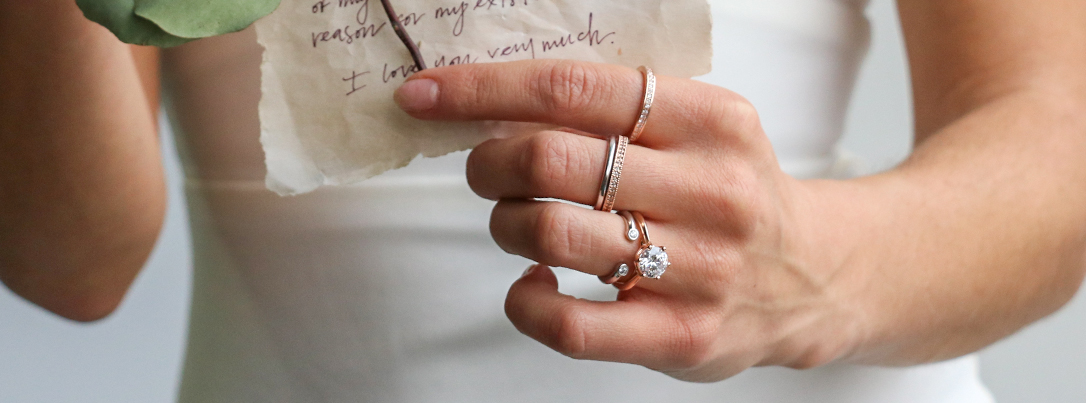 stacked engagement ring and wedding band while holding vows and rose stem