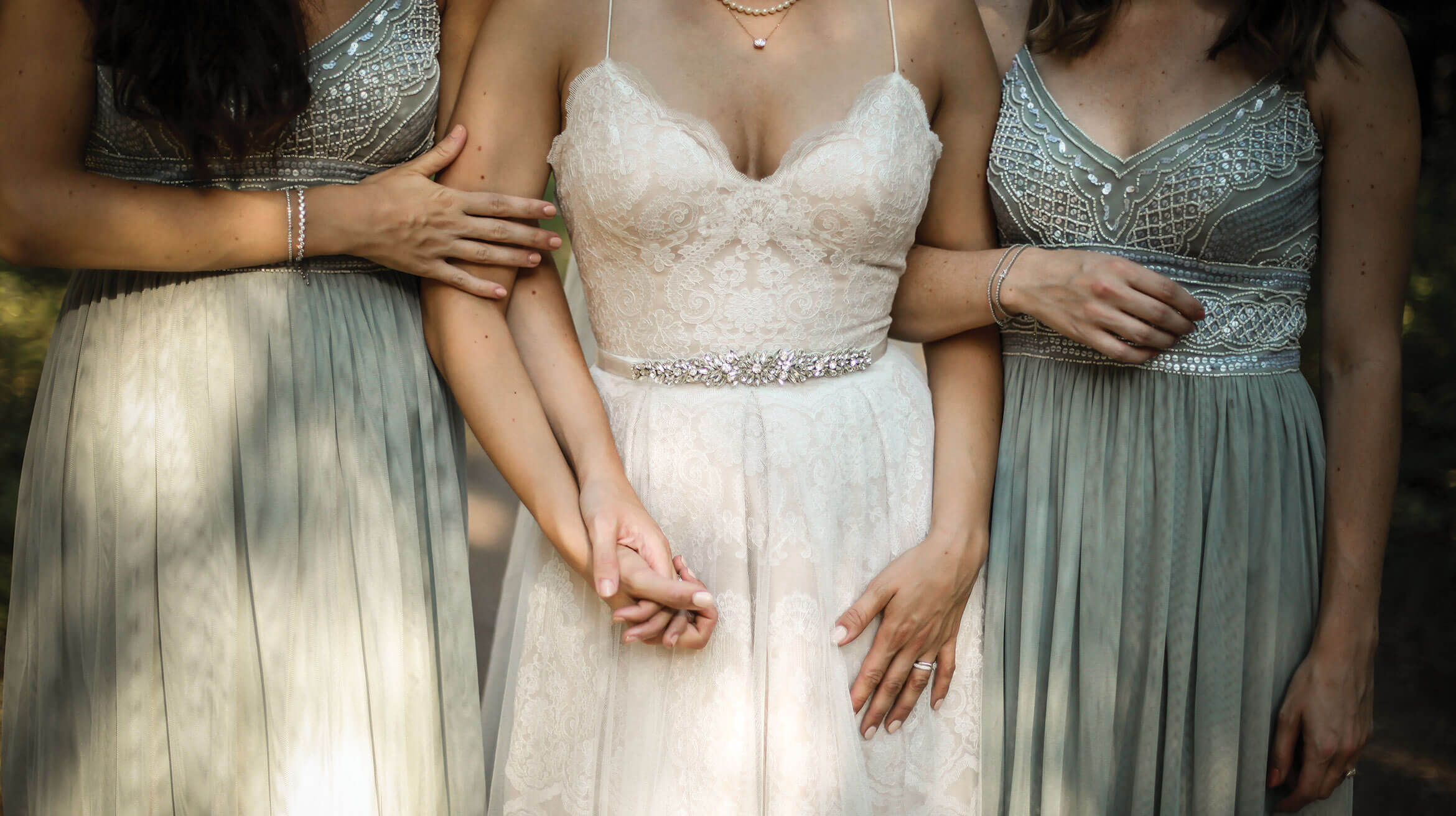 A bride and two bridesmaids holding hands before the ceremony.