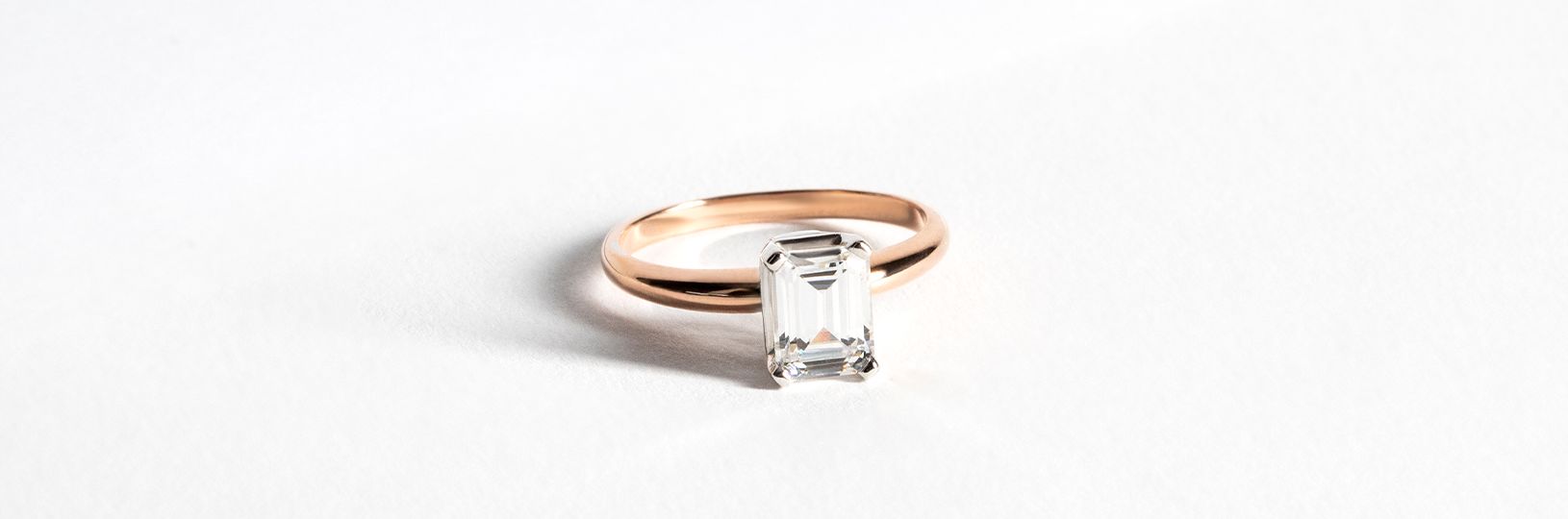 A solitaire rose gold engagement ring with an emerald cut stone