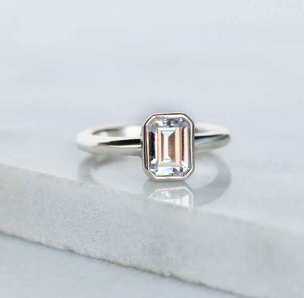 An emerald cut stone in a bezel engagement ring setting